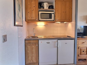 A compact kitchen with wooden cabinets, a microwave, a sink, and a dishwasher.