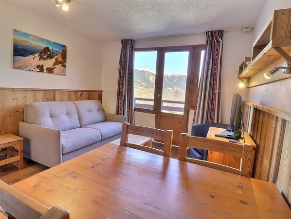 A cozy room with a wooden dining table, a sofa, and a painting of a mountain landscape.