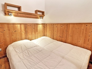 A bed with a wooden headboard, a wall-mounted shelf, and a light fixture.