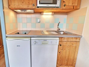 A compact kitchen with wooden cabinets, a microwave, a dishwasher, and a tiled backsplash.