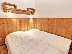 A bed with a wooden headboard, a wall-mounted shelf, and a light fixture. - Comfortable 2-Room, 4 Pers, Ski-In, Close to Shops (La Tania)
