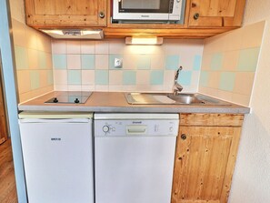 A compact kitchen with wooden cabinets, a microwave, a dishwasher, and a tiled backsplash. - Comfortable 2-Room, 4 Pers, Ski-In, Close to Shops (La Tania)