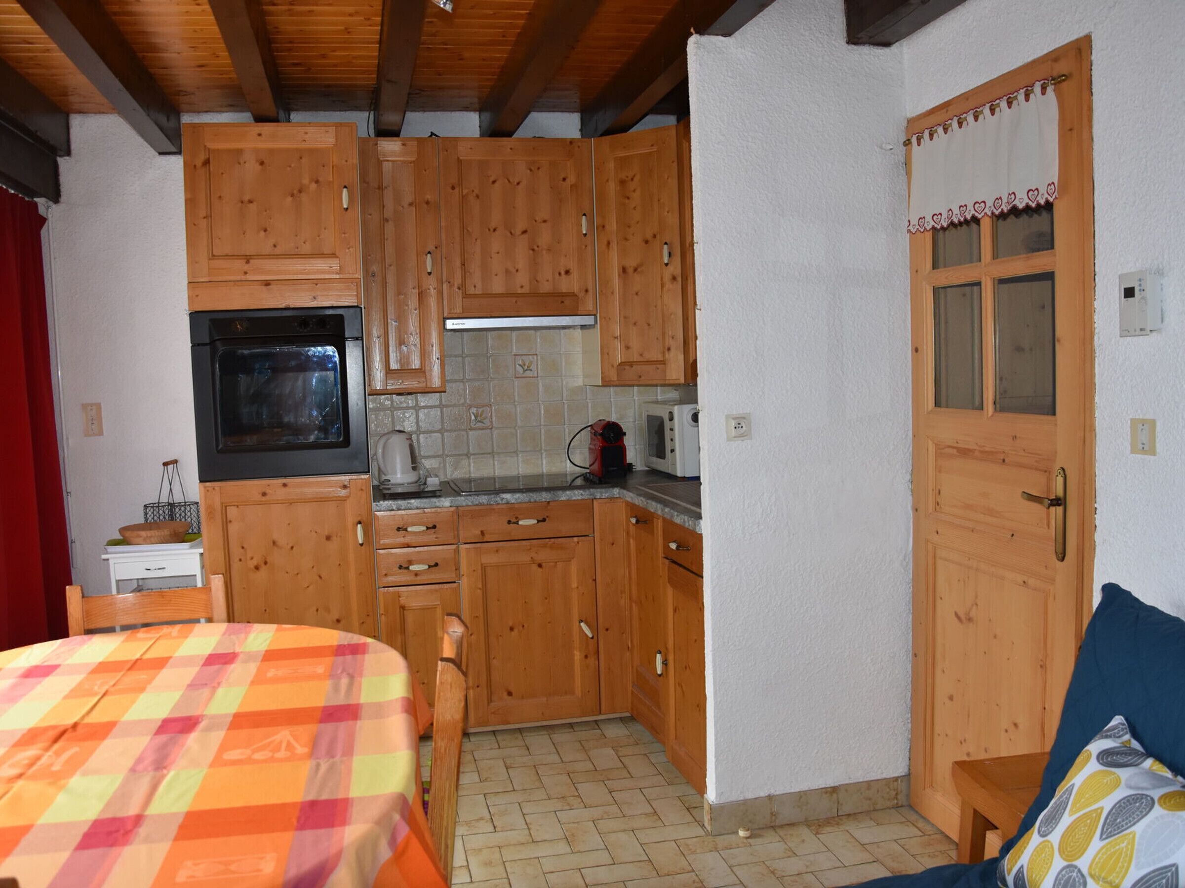 Une cuisine compacte avec des meubles en bois, un four à micro-ondes et une cuisinière. On y trouve une table à manger avec une nappe colorée et une chaise.