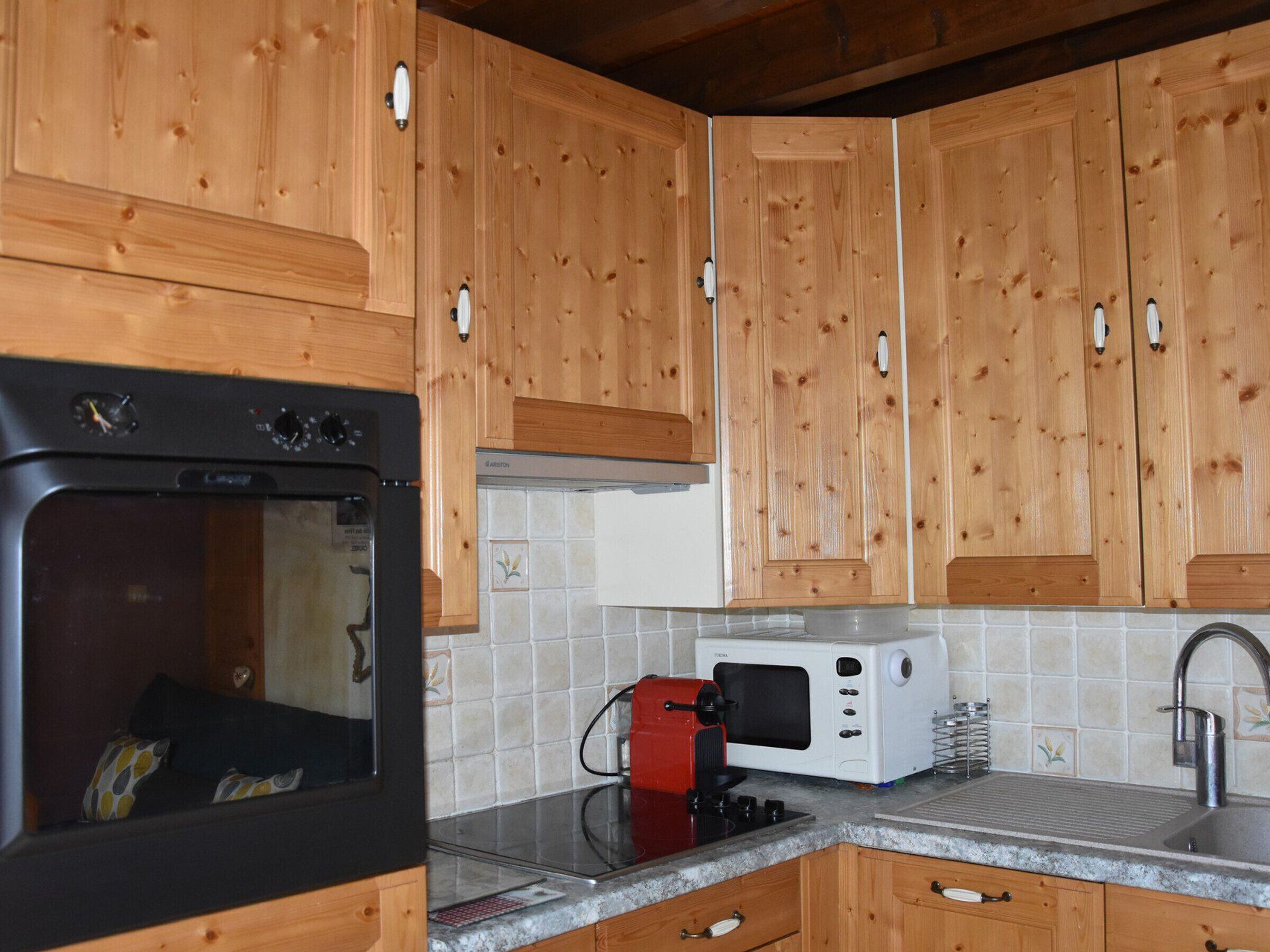 A kitchen with wooden cabinets, a black oven, a red toaster, a white microwave, and a stainless steel sink.