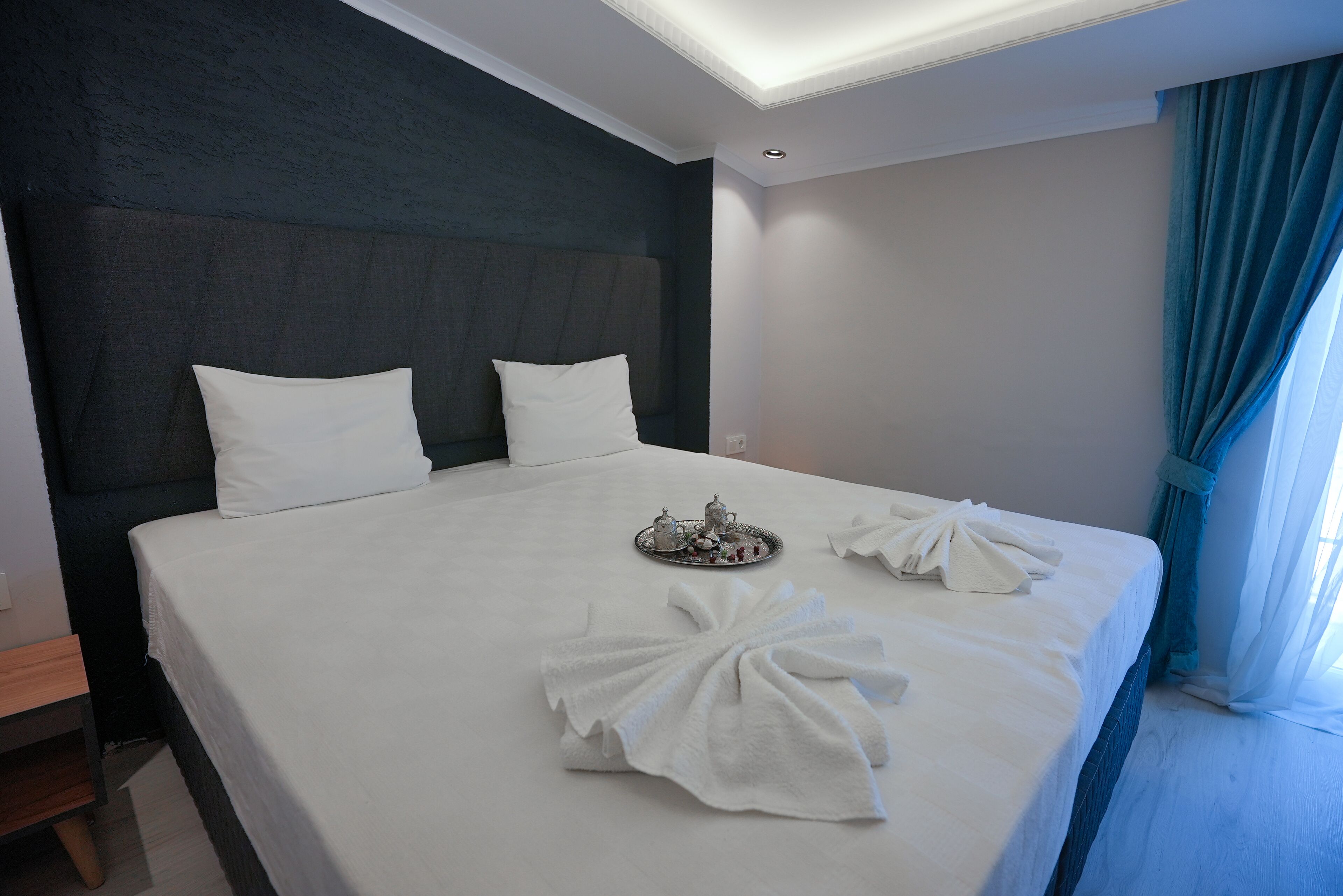 A neatly made bed with white linens, a tray with tea and sugar, and towels arranged on the bed.