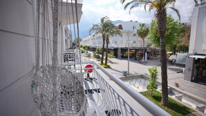 Un balcon orné de décorations en macramé, une vue sur une rue bordée de palmiers et un immeuble sur lequel on peut lire l’inscription « TEL ».