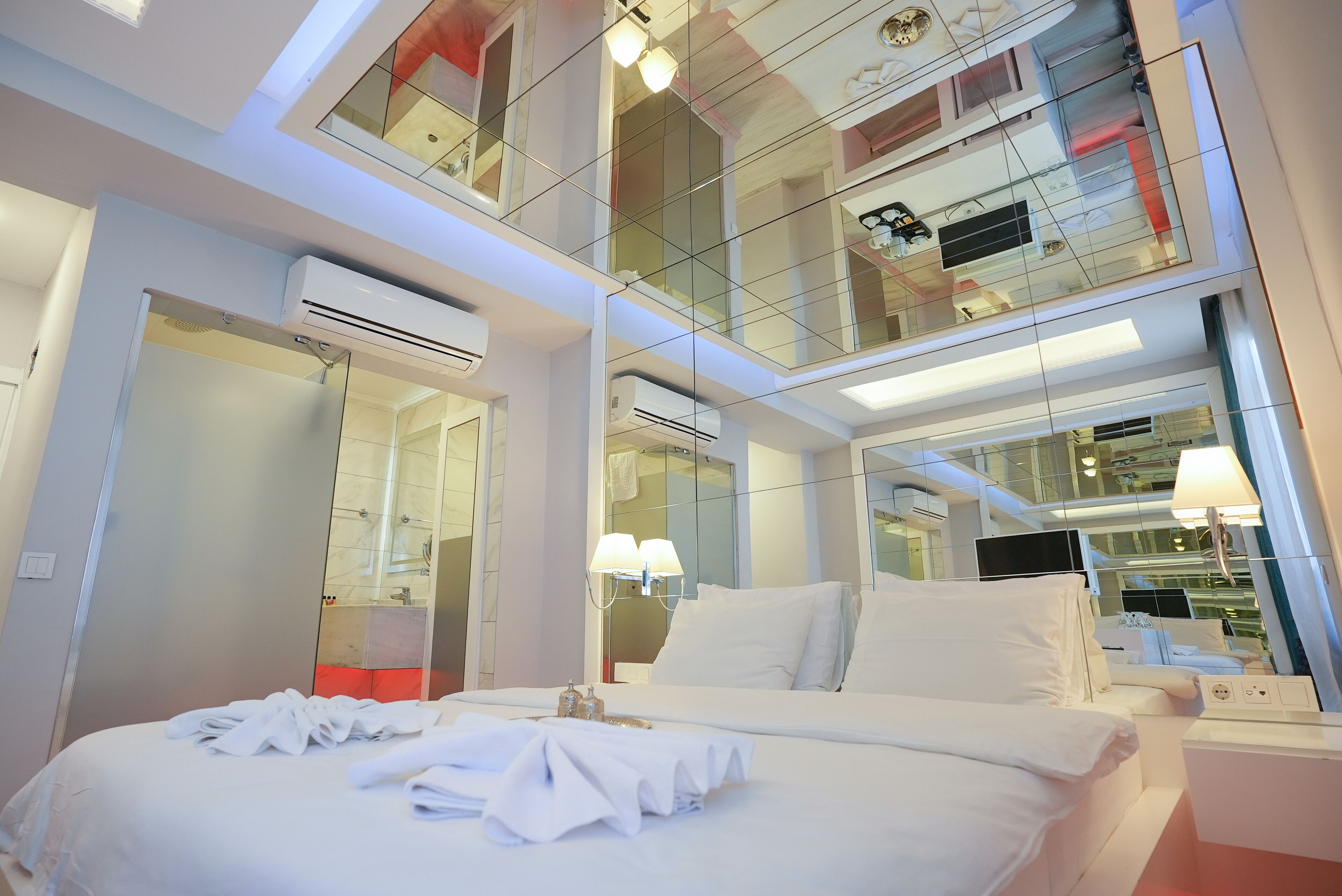 A modern hotel room with a large bed, a glass-enclosed balcony, and a well-lit bathroom.