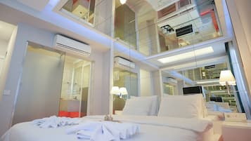 A modern hotel room with a large bed, a glass-enclosed balcony, and a well-lit bathroom.