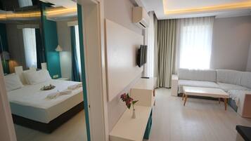 A modern hotel room with a bed, a sofa, a small table, and a TV.