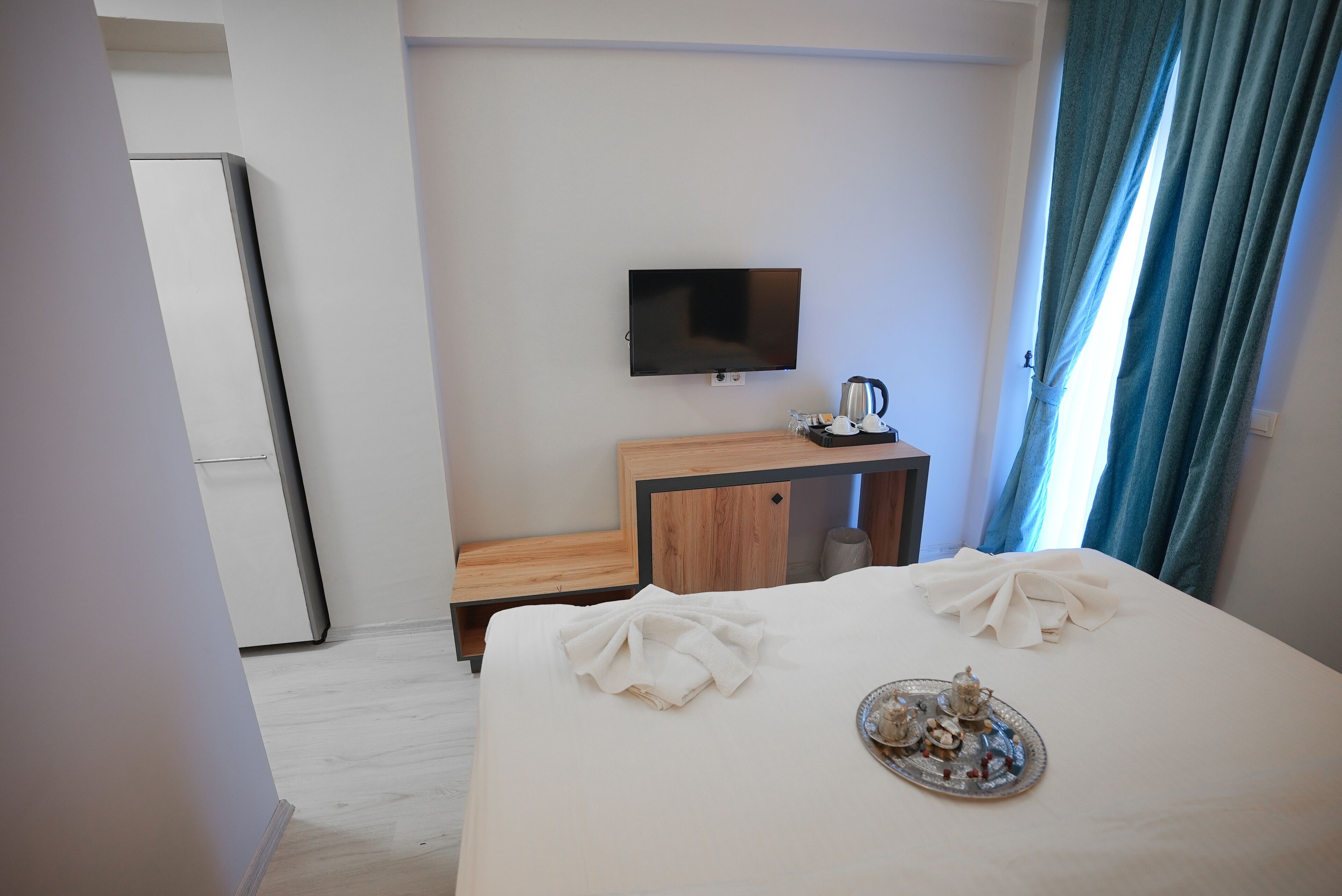 A hotel room with a bed, a TV, a small wooden table, and a tray with tea and pastries.