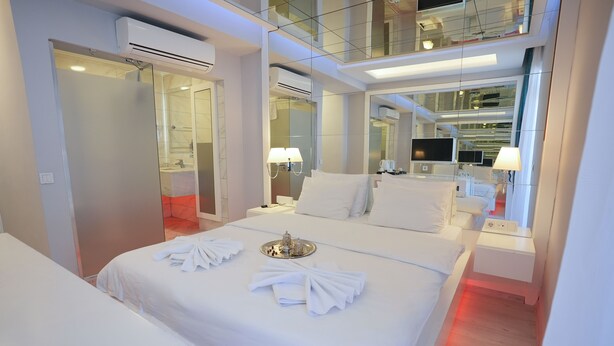 Une chambre d’hôtel moderne avec un grand lit, une table de chevet avec une lampe, une télévision et un miroir.