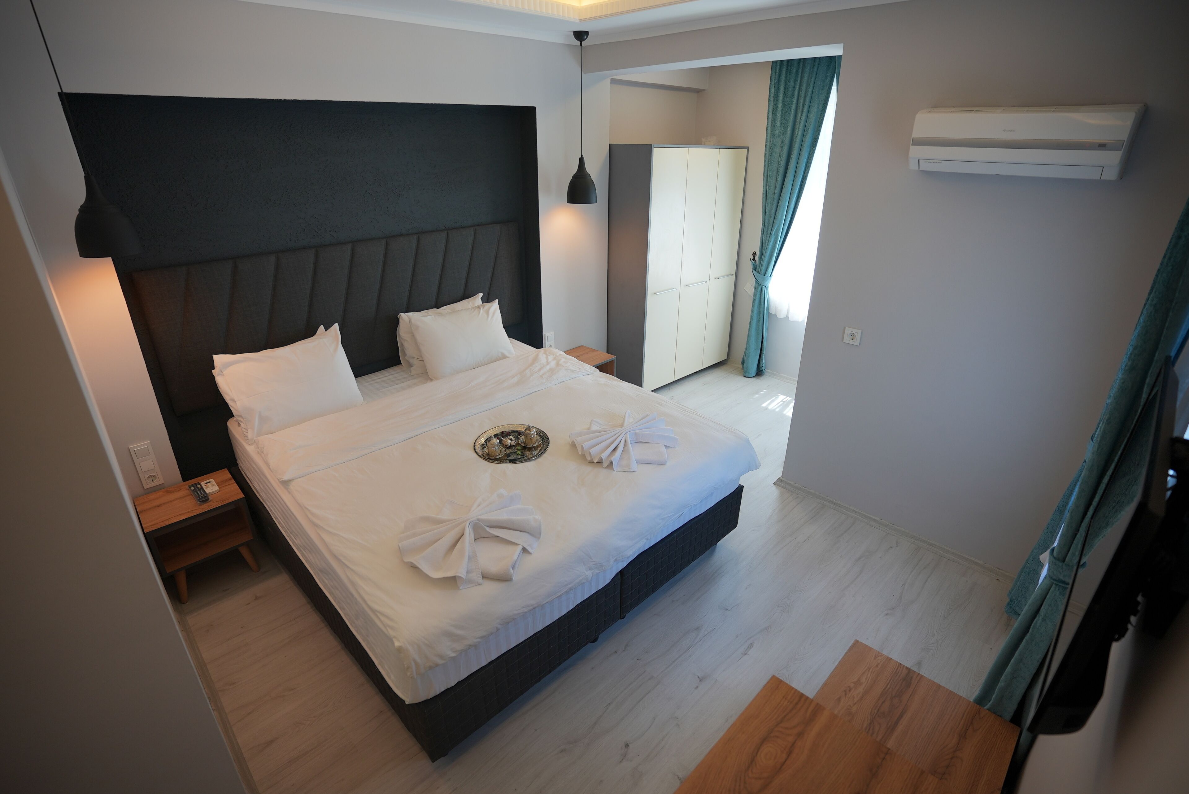 A modern hotel room with a large bed, bedside tables, a wardrobe, and an air conditioning unit.