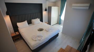 A modern hotel room with a large bed, bedside tables, a wardrobe, and an air conditioning unit.