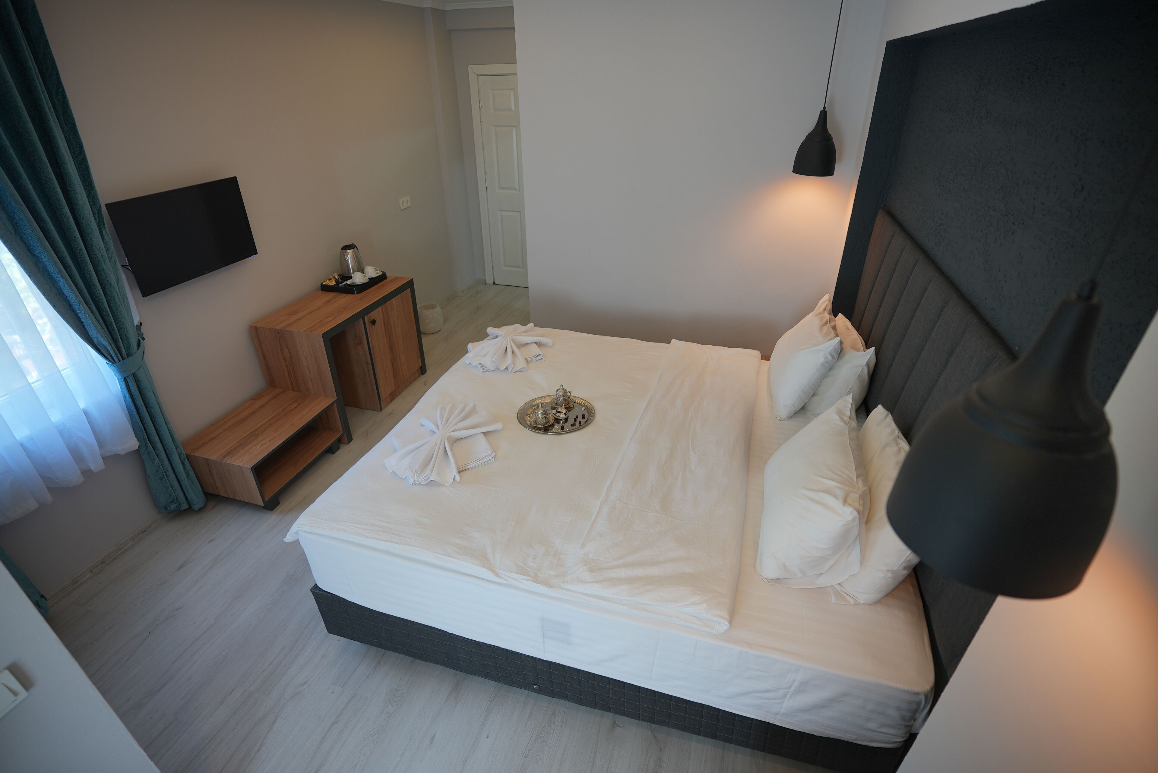 Una cama bien hecha con almohadas y una bandeja, una mesita de noche con lámpara, y un televisor montado en la pared.