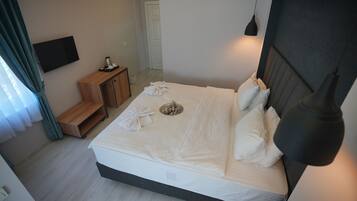 Una cama bien hecha con almohadas y una bandeja, una mesita de noche con lámpara, y un televisor montado en la pared.
