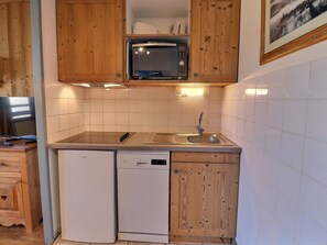 A compact kitchen with wooden cabinets, a built-in microwave, a dishwasher, and a sink. - Comfortable 2-Bedroom, Ski-In/Ski-Out, Near Shops (La Tania)