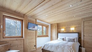 Ett sovrum med träpanel på väggarna, en säng, två sänglampor, en tv som är monterad på väggen och ett fönster med utsikt över träd.