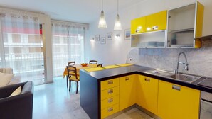 A modern kitchen with yellow cabinets, a black countertop, and a dining area with a table and chairs. - Spacious 1-bedroom with AC, terrace and private garage near the sea (Menton)