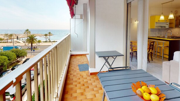 A balcony with a view of the beach, a small table with fruits, and a kitchen area visible through an open door. - Spacious 1-bedroom with AC, terrace and private garage near the sea (Menton)