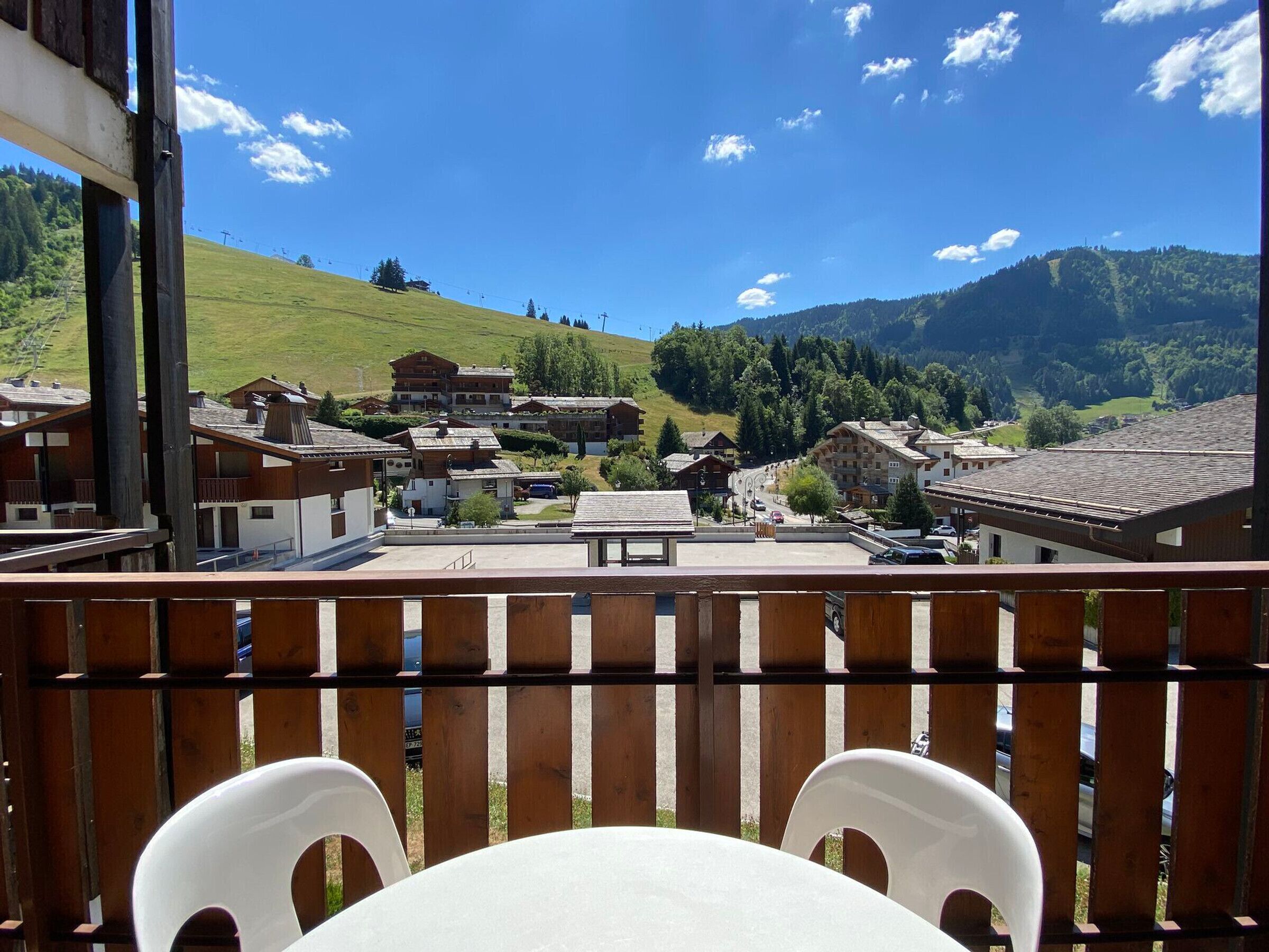 A balcony with wooden railings overlooking a village with traditional buildings and a mountain backdrop.