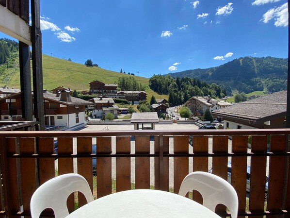 A balcony with wooden railings overlooking a village with traditional buildings and a mountain backdrop.
