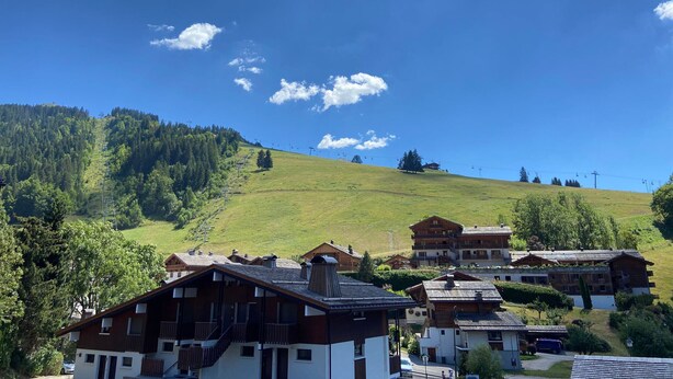 Ein Bergferiendorf mit Chaletbauten, einer Seilbahn und blauem Himmel.
