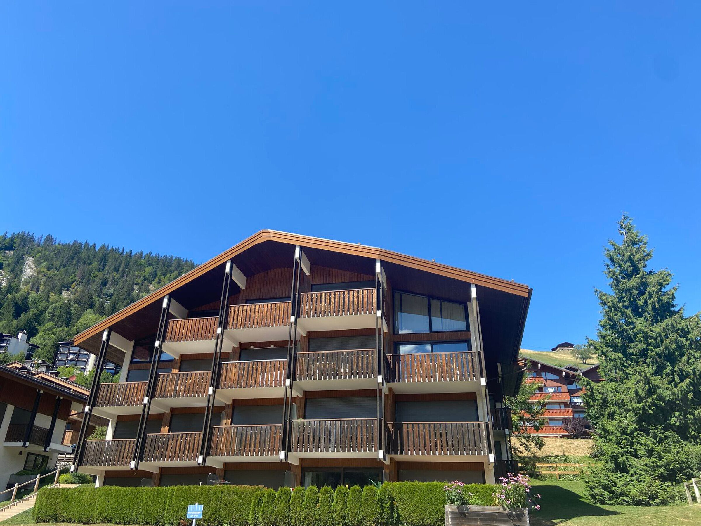 Un hotel de varios pisos con balcones de madera y un paisaje montañoso al fondo.
