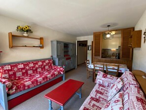 Una sala de estar con un sofá rojo, un banco rojo y un comedor con una mesa y sillas de madera.
