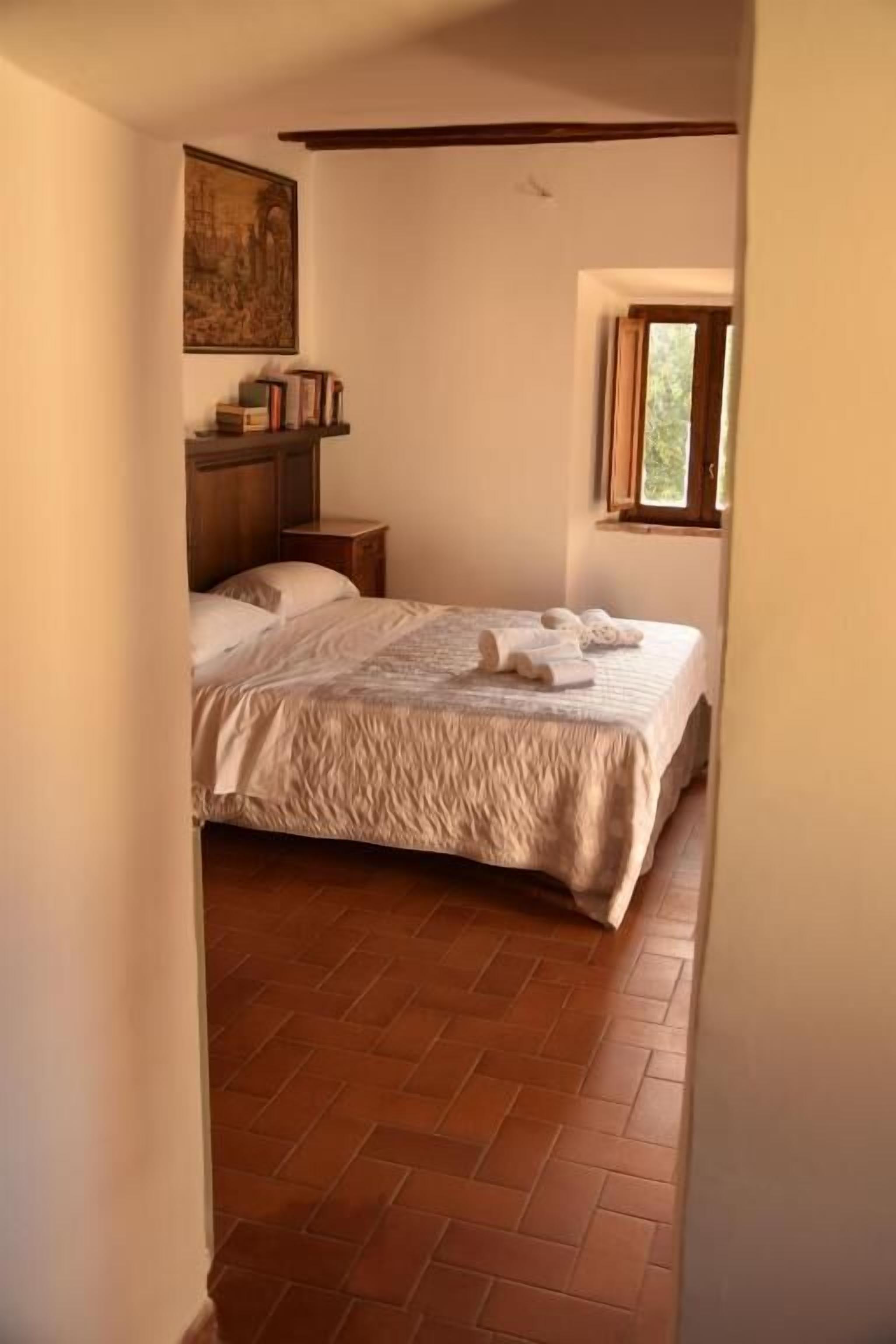 A bedroom with a bed, a nightstand, a painting on the wall, and a window.