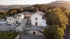 A white building with a bell tower, surrounded by trees and hills. - Convento dei Cappuccini (Tolfa)
