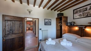 A bedroom with a wooden door, a bed with white linens, a radiator, and a wall-mounted shelf with books. - Convento dei Cappuccini (Tolfa)