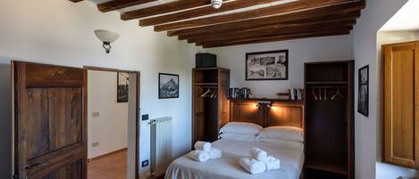 A bedroom with a wooden ceiling, a bed with white linens, a radiator, and a wooden wardrobe.