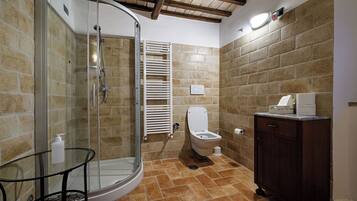 A bathroom with a glass shower enclosure, a toilet, a sink with a cabinet, and a towel rack.