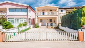 A two-story residential building with a balcony, a gated entrance, and a paved driveway. - Apartment Bubanovic (Vir)