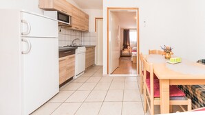 A modern kitchen with white cabinets, a microwave, and a dishwasher. There is a dining area with a wooden table and chairs. - Apartment Bubanovic (Vir)
