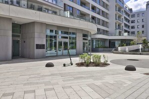 Stylish building with a curved facade, large windows, and a flat roof, set amidst a paved area with lush greenery.