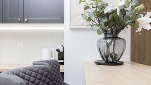 A modern kitchen with a grey upholstered chair, a clear vase with white flowers, and a wooden table.