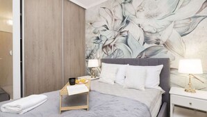 A modern hotel room with a large bed, a wooden nightstand, a bedside table, and a floral mural on the wall.