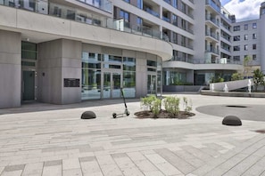 Un bâtiment moderne doté d’une façade incurvée, de grandes fenêtres et d’une cour pavée agrémentée de bornes et de petites plantes.
