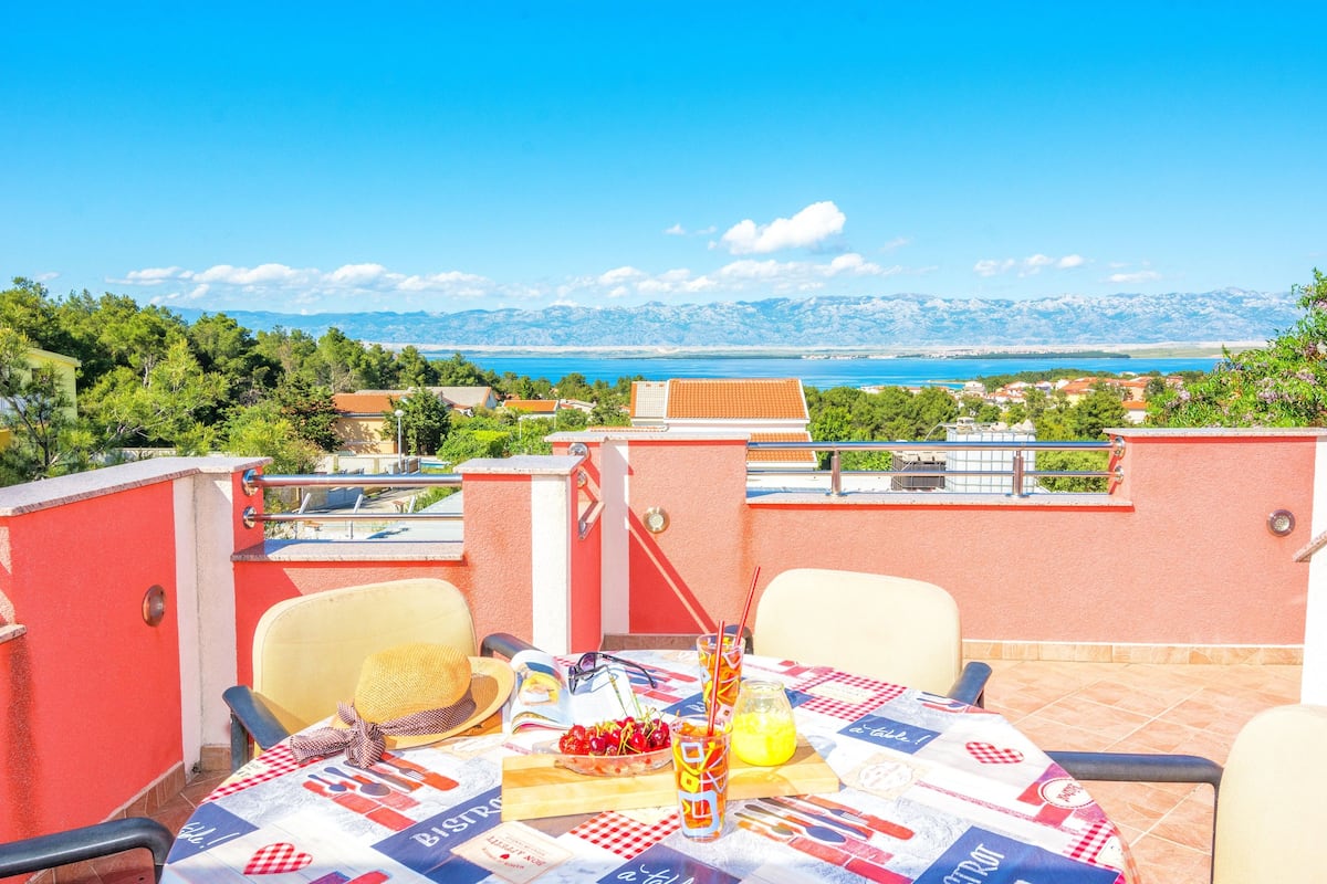 Una terraza con mesa lista para dos, con vistas panorámicas de la costa y montañas al fondo.