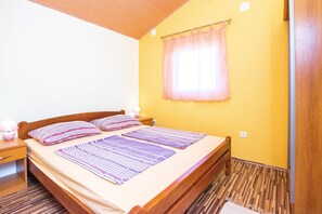 Une chambre à coucher avec un lit en bois, une table de chevet, une lampe et une fenêtre ornée d’un rideau léger.