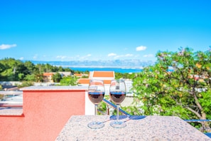 Deux verres à vin sont posés sur une table, offrant une vue sur un paysage montagneux et une étendue d’eau en arrière-plan.