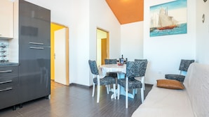 A compact living space with a dining area, a sofa, and a kitchen with a modern refrigerator. - Apartments Kopi (Vir)