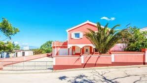 A red building with a white door and window shutters, surrounded by a fence and palm trees. - Apartments Kopi (Vir)