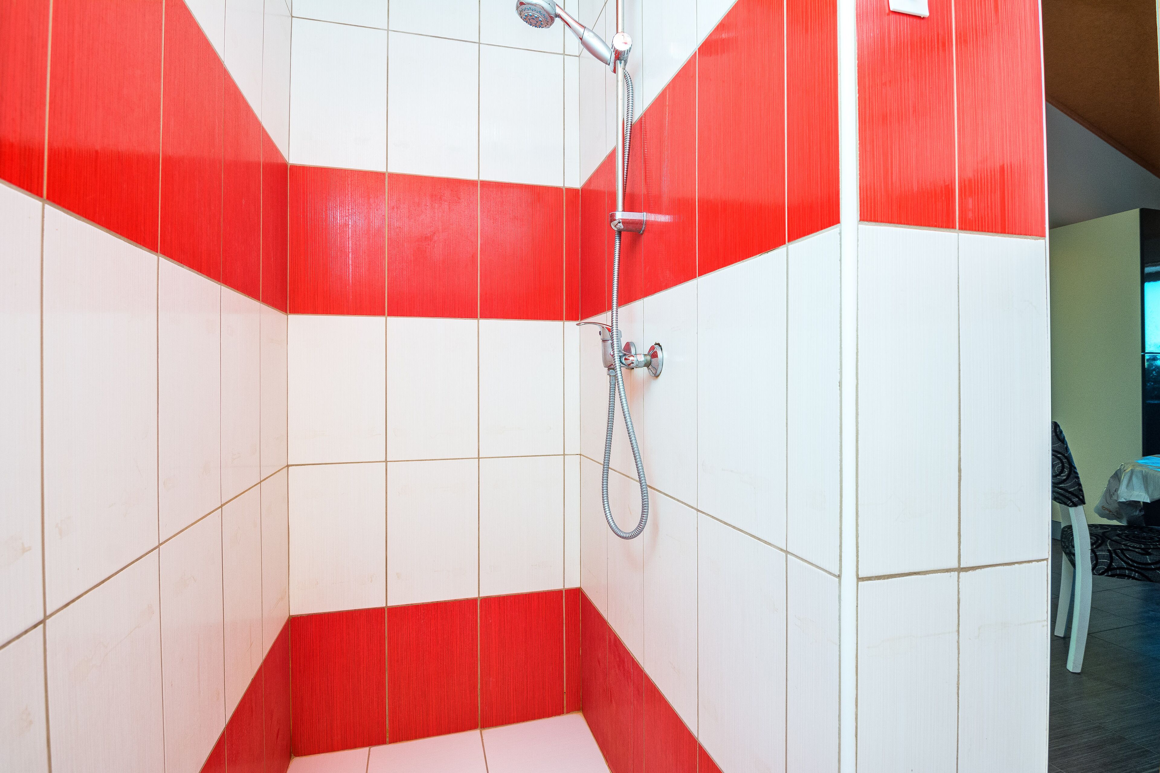 Ein Badezimmer mit rot-weiß gefliesten Wänden, einer Duschkabine und einem Stuhl in der Ecke.
