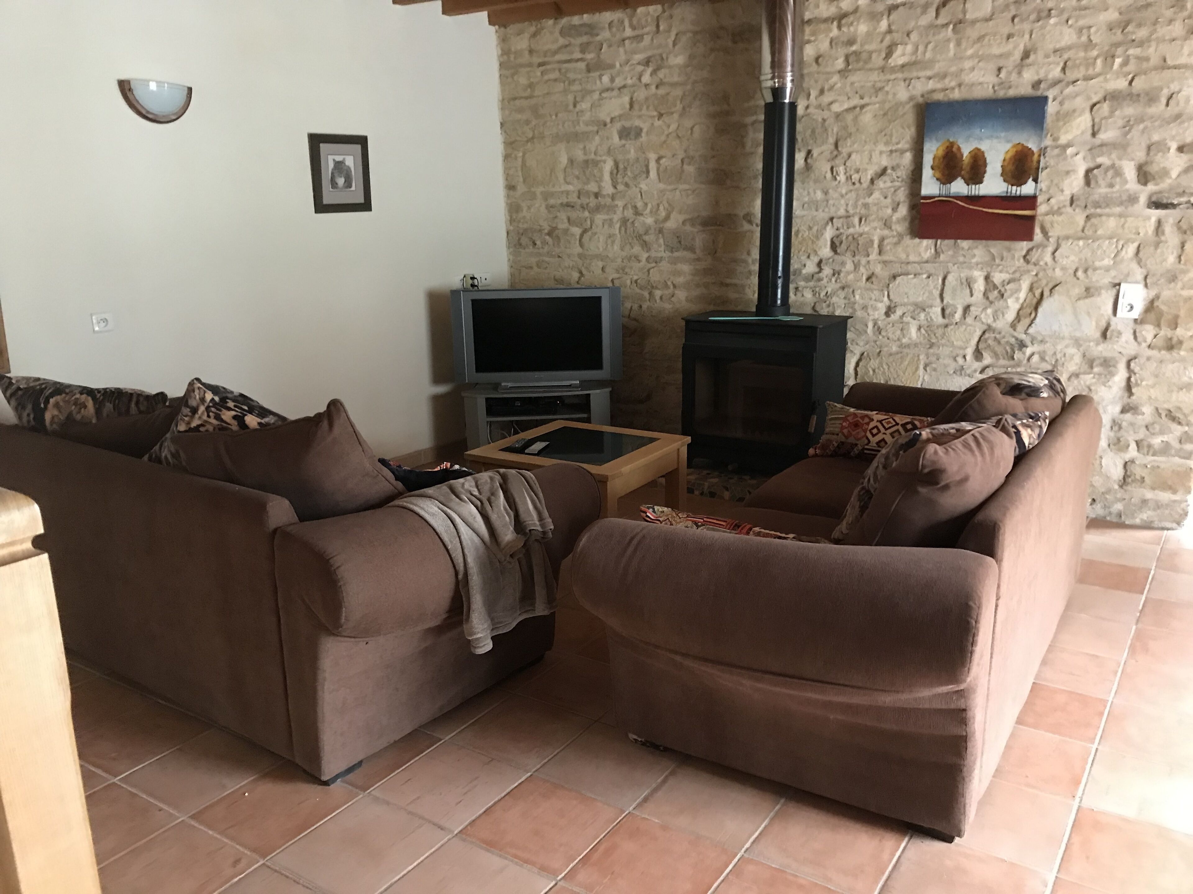 Una sala de estar con dos sofás marrones, un televisor, una chimenea y una pared de piedra.