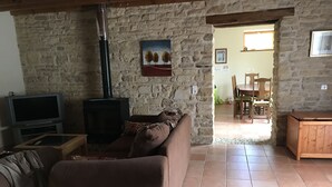 Un saló acollidor amb una paret de pedra, una llar de foc, televisió i zona de menjador amb cadiretes i taula.