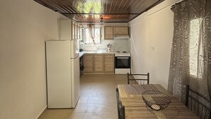 A compact kitchen with wooden ceiling, a dining table, and a refrigerator. - Antigoni Apartments (Corfu)