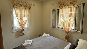 A bedroom with a bed, two windows with curtains, a bedside table, and a nightstand. - Antigoni Apartments (Corfu)