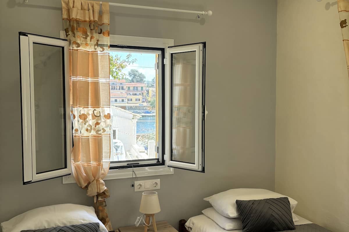 Une chambre avec deux lits, une table de chevet, une lampe et une fenêtre avec des rideaux.